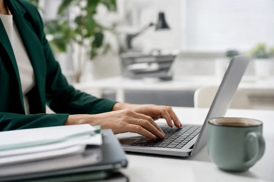 Dłonie na klawiaturze laptopa obok uporządkowanych dokumentów