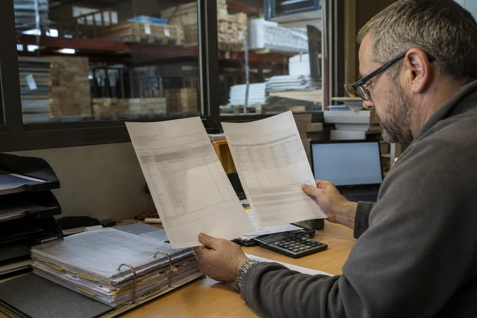 Księgowy w hurtowni przegląda listę zaległych faktur i dwie oferty biur informacji gospodarczej